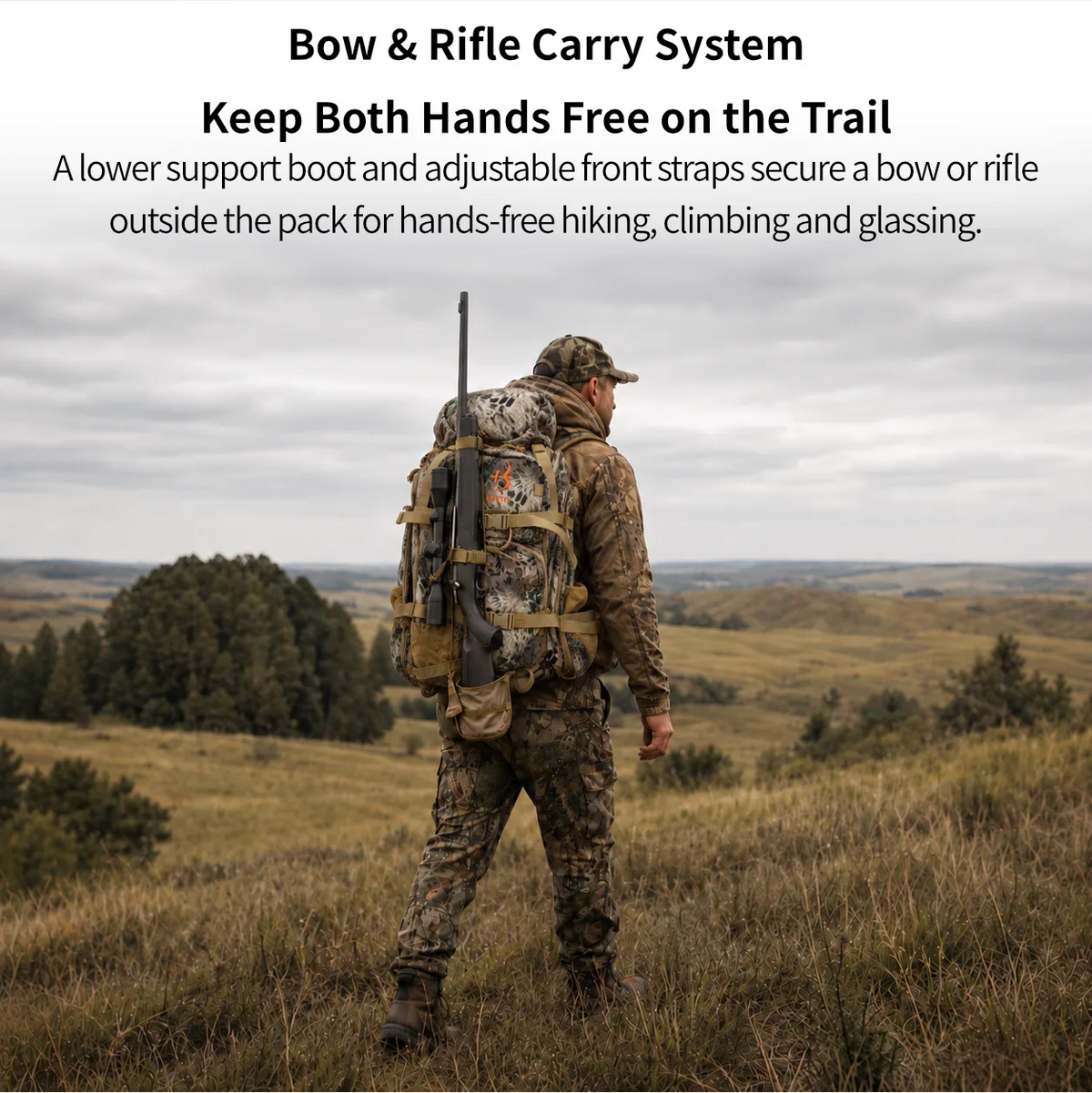 A man in camouflage outdoor gear stands on a grassy hill wearing a large bow and rifle backpack, with text at the top reading 'Bow & Rifle Carry System' and 'Keep Both Hands Free on the Trail.'.